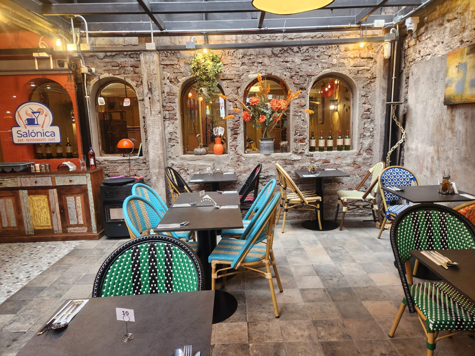 Terraza empedrada de Salónica con mesas, flores y luces cálidas